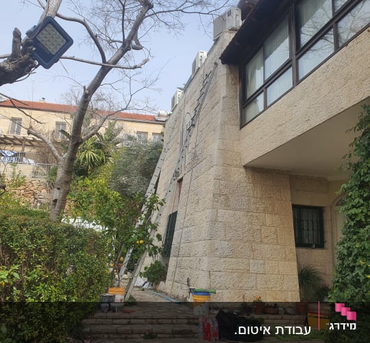 ציוד איטום וסולמות מוצבים לצד קיר חיצוני של בית פרטי